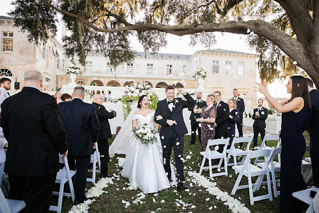 bride and groom cheering and walking out of ceremony with white rose petals