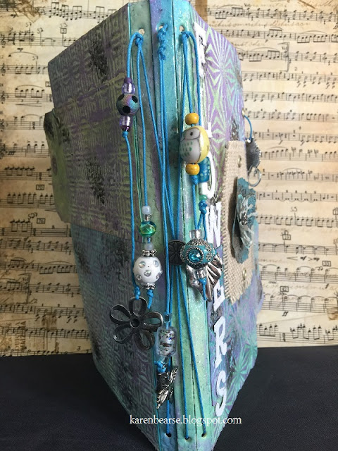 Spine of the journal with lots of beads in blues, greens hanging from cobalt hemp with flower & butterfly charms.