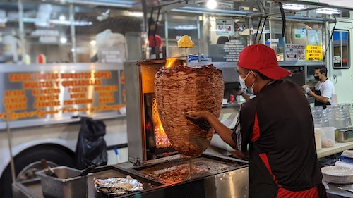 A taquero cuts al pastor meat from the trompo