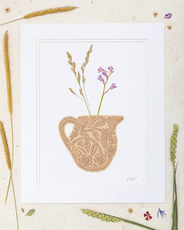 matted yarn embroidered pitcher containing stalks of dried flowers