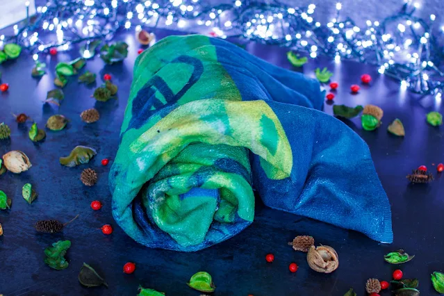 A blue and green soft towel rolled up, but with a child's artwork design of dragon wings on