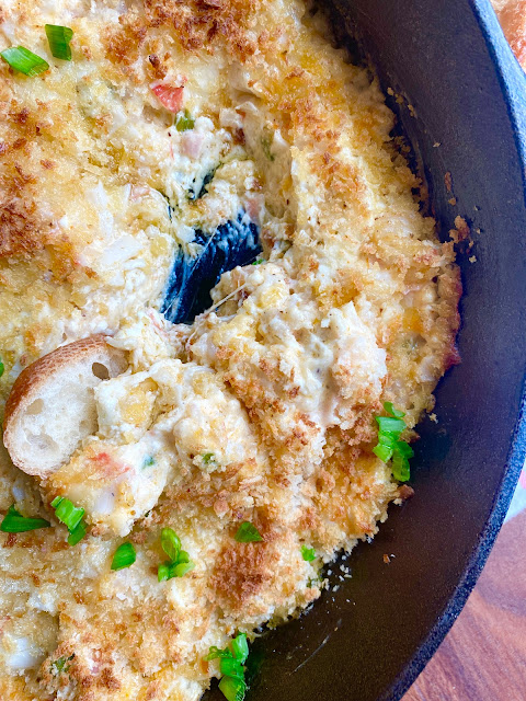Close up of seafood dip in a cast iron skillet with a scoop of the dip moved with a baguette slice.