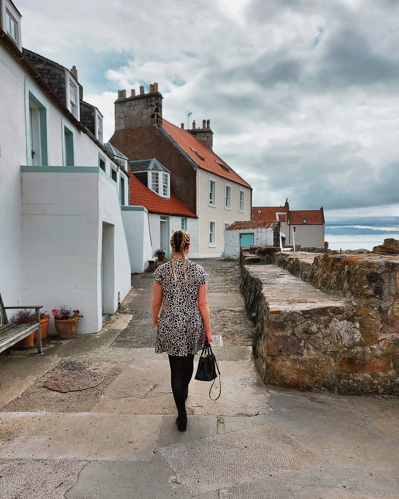 Woman with plaits and leopard print dress walking along the West Shore in Pittenweem