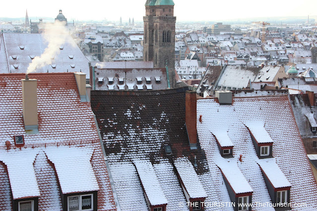 A tall green church spire and a sea of red rooftops covered in a light dusting of fresh snow.