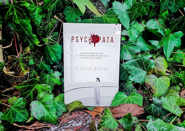 na zdjęciu w otoczeniu zielonych liści bluszczu stoi książka "Psychopata" z białą minimalistyczną okładką i czerwonymi elementami.