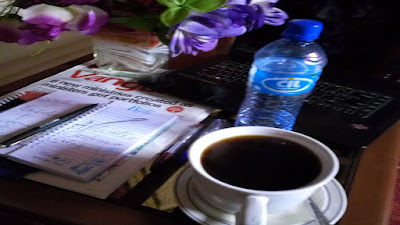 Home business work station with notepad and pen, a bottle of water, computer, flowers and a white mug of coffee.