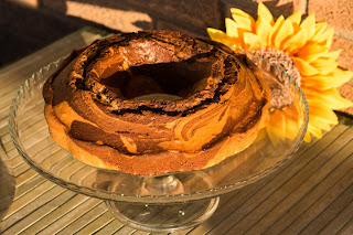 la ciambella variegata al cacao, su alzata portadolci in vetro, con sfondo rustico in mattoni e girasole.