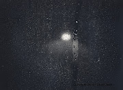 A street light shines through the dark and outlines the rain drops on a .