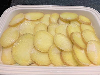 Sliced potatoes on top of chicken bake in a cream coloured casserole dish.