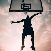 A person performing a vertical jump with outstretched arms, aiming for a basketball hoop.