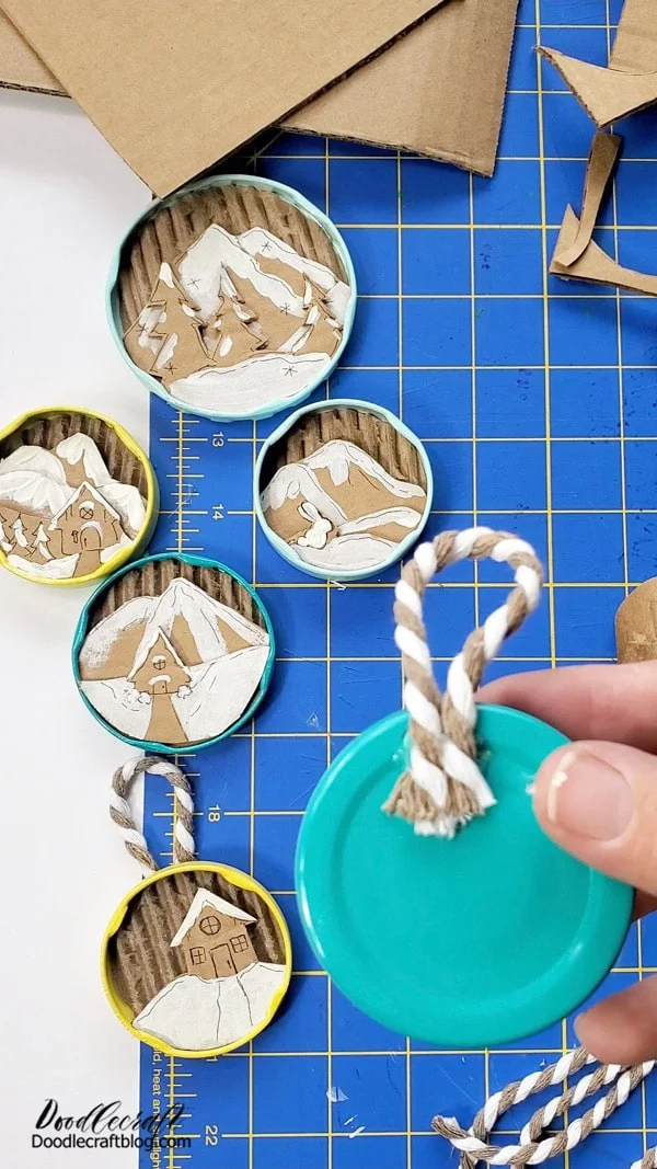 Step 7: Add Twine  Finish off the darling little Winterscape diorama jar lid ornaments with a piece of twine hot glued on the backside of the lid.   You could use thick string, fishing line, yarn, ribbon, an open paper clip, an ornament hook, a hairband...whatever you have already on hand.   You could tie a bow with ribbon to add one more element if desired.