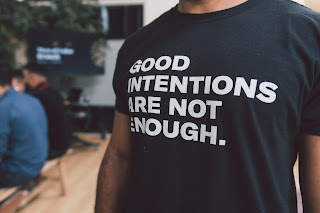 Close up of person in t-shirt that says "good intentions are not enough"