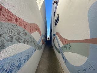 A narrow alley with a mural of hand prints along the length of each side of the walls.