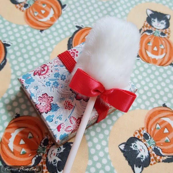 small floral box of blusher with white fluffy makeup puff on stick sitting on top