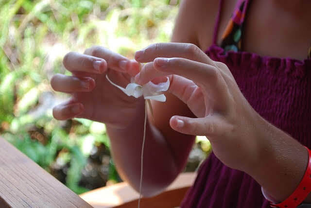 A Little Girl Is Making A Lei With Flowers.