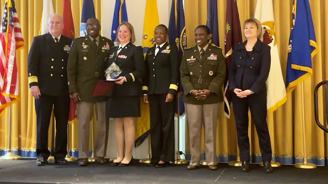 Col. (Dr.) Ashley Maranich (pictured center left, holding award) accepts an award with others in uniform on each side of the stage.