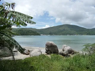 Playa pequeña al costado de la ruta en Porto Belo, con bananeros, rocas grandes, veleros anclados en el agua.