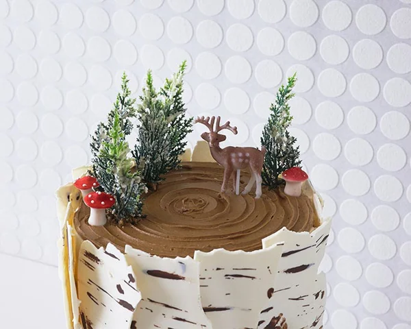     Spread a little buttercream on the pine trees so they look snowy. Place trees, deer and mushroom on top of cake to finish. 