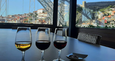 3 copos de vinho do Porto e pires com chocolate, numa mesa de frente para a ponte Luiz I e cidade do Porto