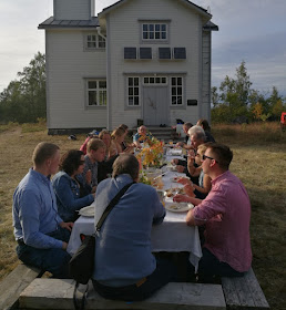 Pitkä pöytä ulkona tutkimusaseman edessä, jonka ääressä noin pari kymmentä ihmistä kesällä. 