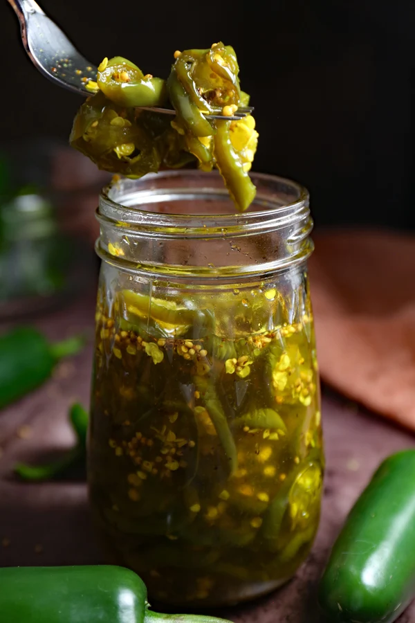 Candied Jalapenos in a Jar: A fork holds a tempting bunch of flavorful jalapenos above a glass jar, perfect for adding a sweet and spicy kick to your dishes.