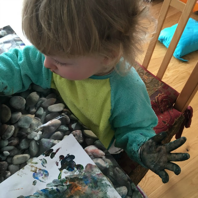 Toddler concentrating and holding hand up covered in murky brown paint