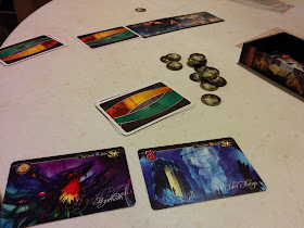 A game of Tides of Madness in progress. Two face up cards are clearly visible in the foreground, with a number of face-down cards and a couple more face up cards visible beyond them. In the centre of the table are some madness tokens.