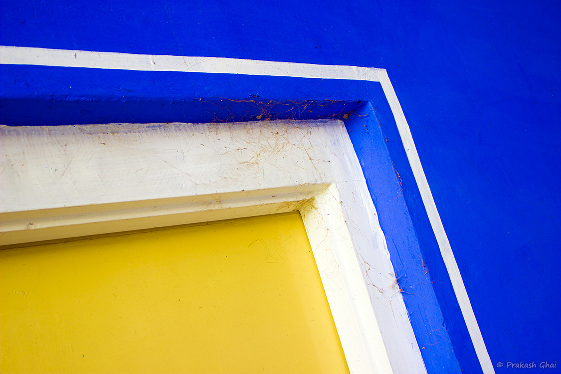 A Minimalist Photo of the Corner of a door depicting geometry and interplay of colors yellow and blue.
