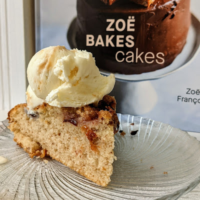 A slice of plum cake topped with ice cream. In the background is the cookbook the recipe comes from - Zoe Bakes Cakes