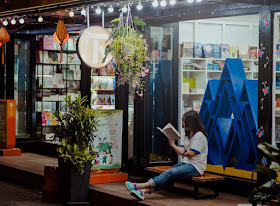 Young woman outside of shop, sitting on bench reading, book