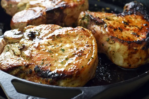 A close-up view of perfectly seared ranch pork chops cooking in a sizzling cast iron skillet.