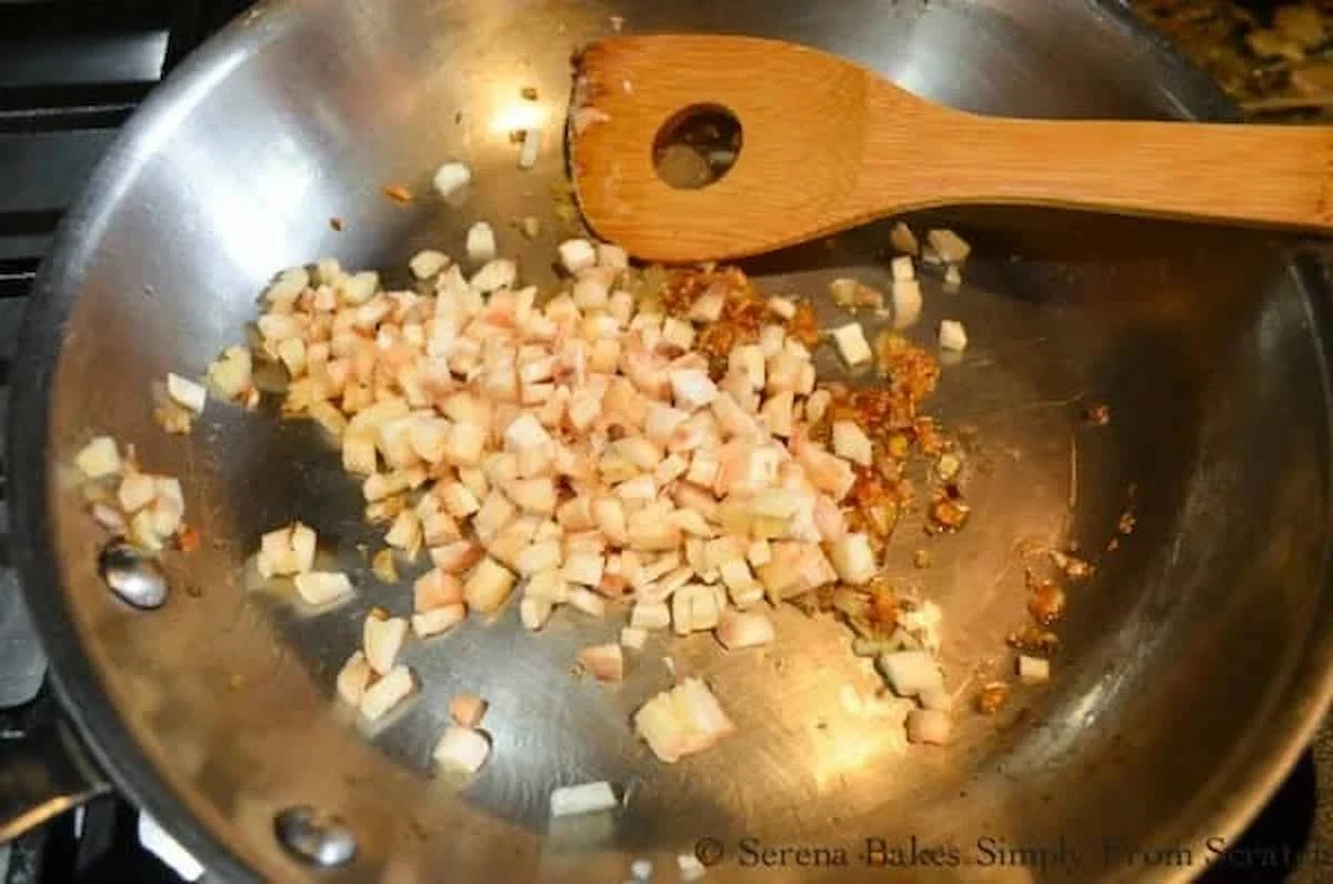 A down shot of caramelized shallot and chopped mushrooms stems in a stainless steel pan.