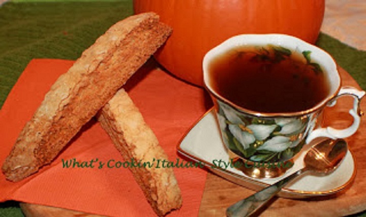 these are pumpkin biscotti Italian cookie with pistachio . They are  on a green and white flowered bup with a demitasse spoon of espresso coffee