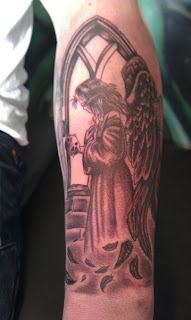 arm tattoo: Angel of Death portrayed as a blindfolded little girl with giant black feathered wings