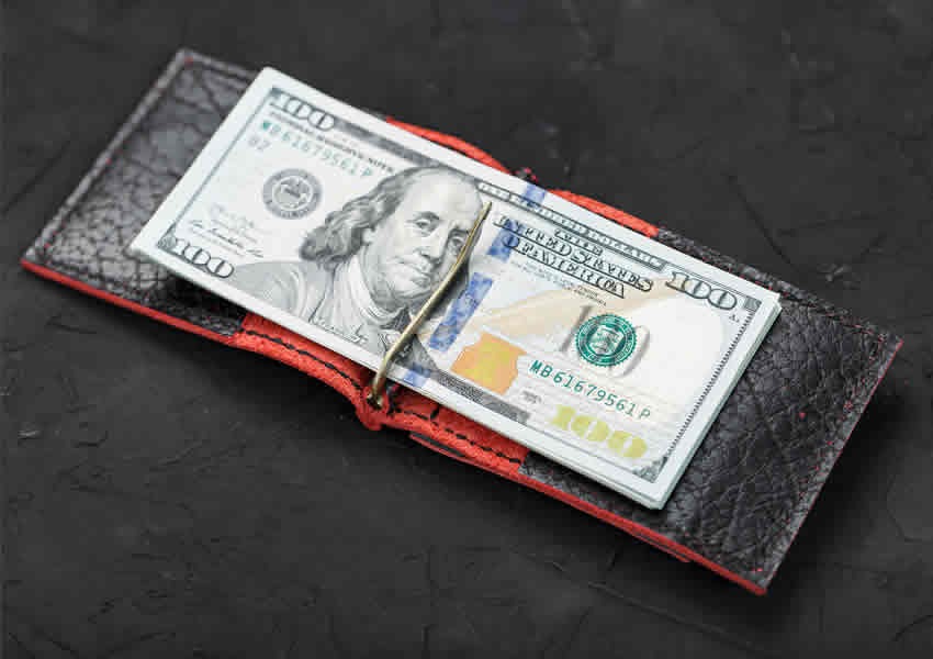 Fundo escuro com uma cédula de dólar sobre uma carteira.
