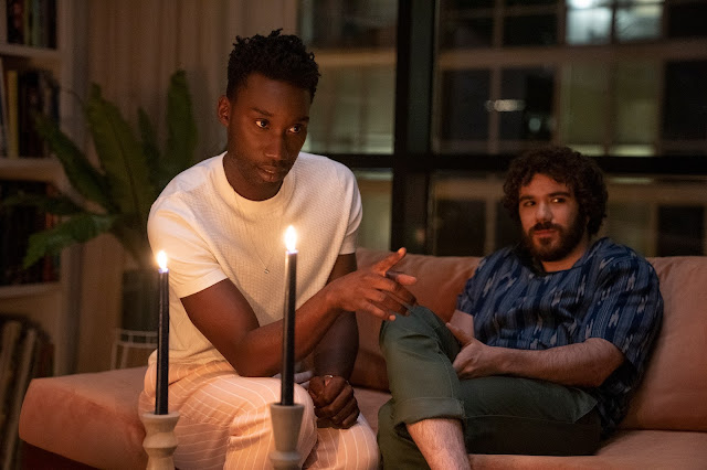 Two men, one Black and one white, tell a story in front of a candle