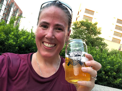 Photo of me post-race. I am sweaty, smiling, and holding a glass of free beer.