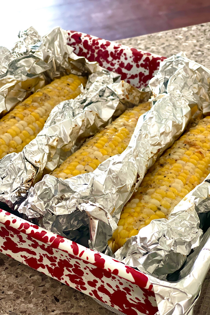 Ears of corn wrapped in foil in a baking pan.