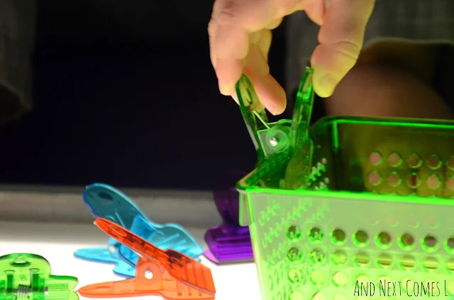 Close up of a toddler's hand squeezing a translucent chip bag clip onto a colorful plastic container