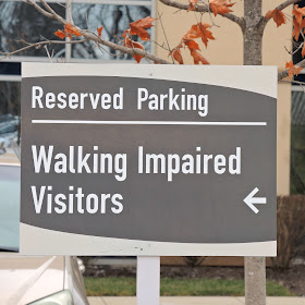 grey sign, reads reserved parking on first line, walking impaired visitors with an arrow pointing backwards on the second 