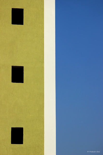 A Colorful look up Minimalist Photograph of Three Windows of a residential apartment in Jaipur City, against clear blue skies.