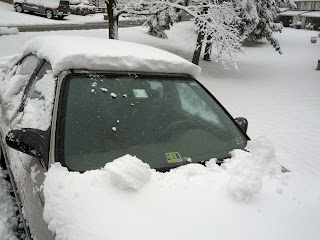 Car is still mostly snow-covered, but the sheet has been removed and the windshield is completely clear.