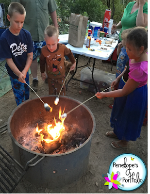 Three children standing around a fire, roasting marshmallows for smores