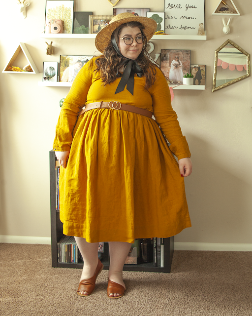 An outfit consisting of a brown panama hat, a mustard yellow long sleeve mock linen midi dress and brown d'orsay sandals.
