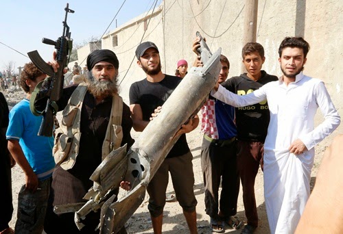 An Islamic State militant (L) stands next to residents as they hold pieces of wreckage from a Syrian war plane after it crashed in Raqqa, in northeast Syria September 16, 2014.