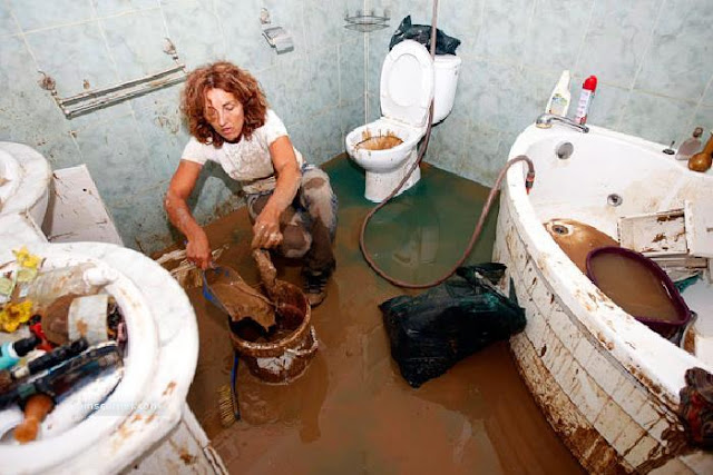 A resident scoops up mud inside her flooded house