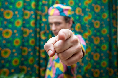 man in a colorful dress points at the camera