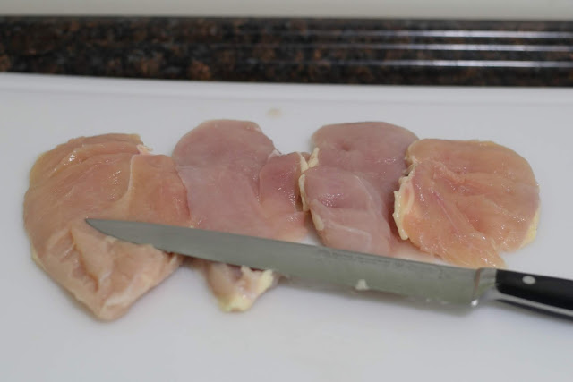 Boneless Skinless chicken breasts, cut in half, on a cutting board with the knife. 