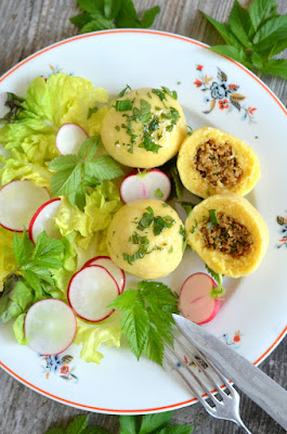 Veggie-Grammelknödel auf einem gemusterten Teller, ein Knödel ist aufgeschnitten, daneben Messer und Gabel. Auf dem Teller liegt noch Salat und Radieschen.