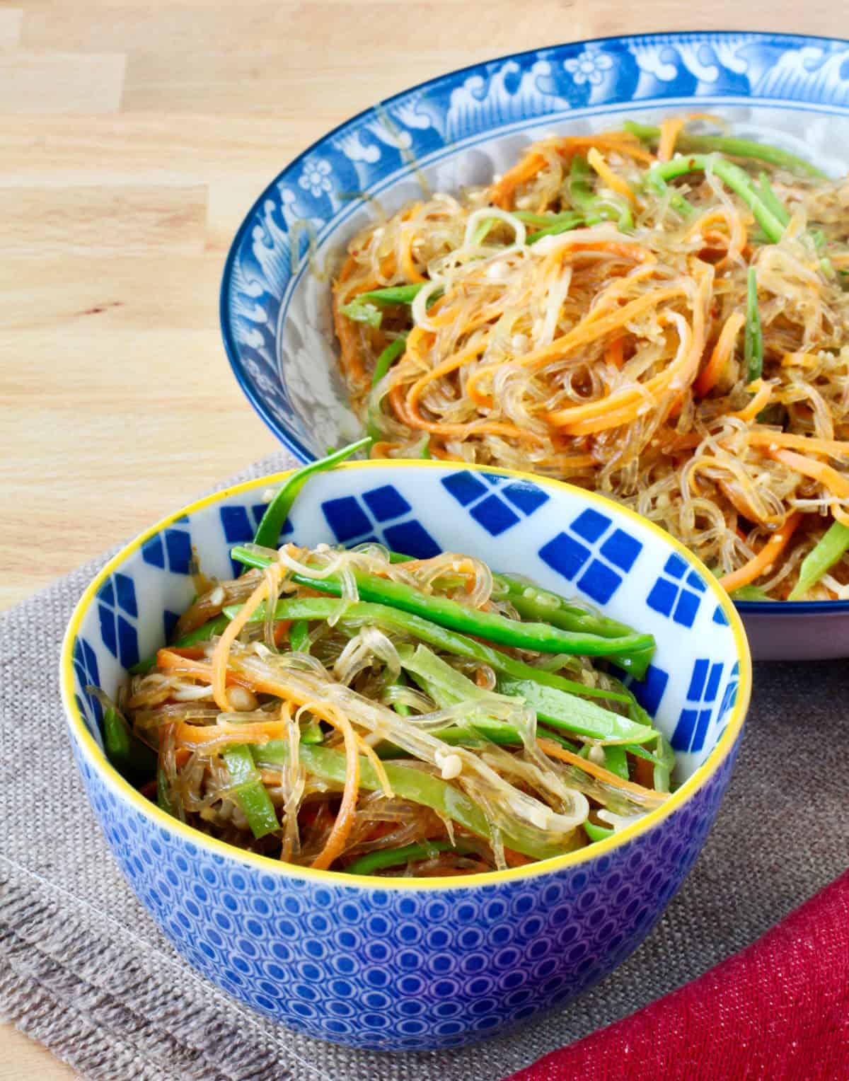 Stir-Fried Cellophane Noodles with Enoki Mushrooms in a small bowl in front of a larger bowl.